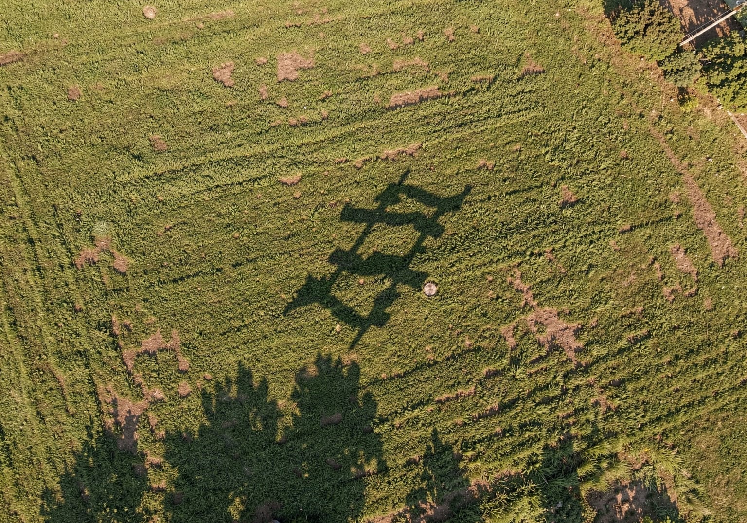 Sombra de un dron sobre un techo verde visto desde arriba durante un vuelo, con luz cálida de atardecer